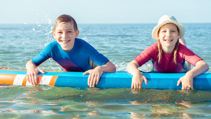 To børn ligger i vandet på et surfboard