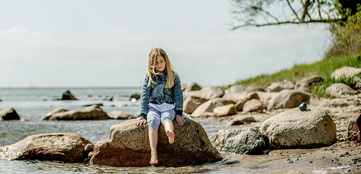 Pige sidder på sten i strandkanten